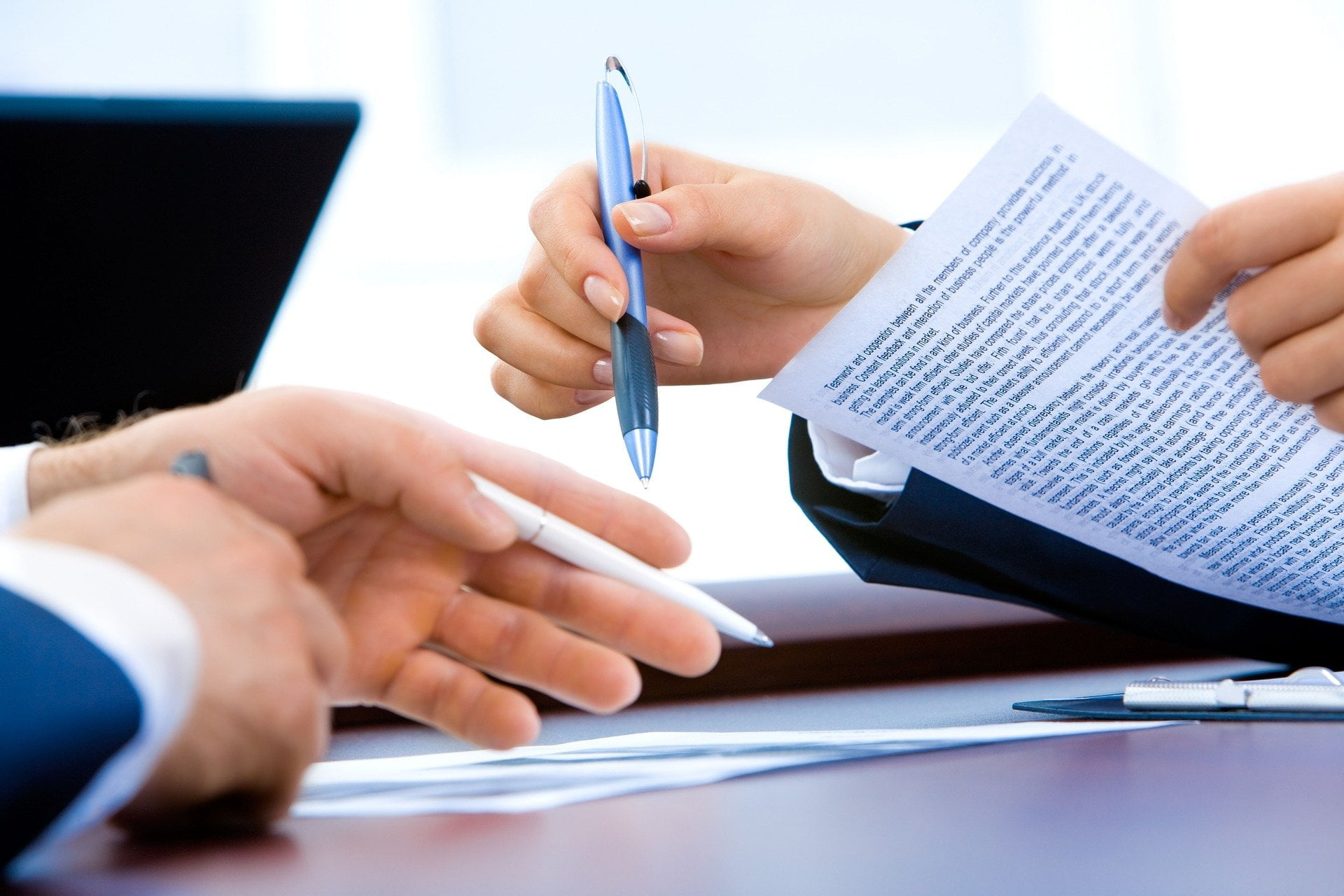 a hand with a pen above a pile of papers